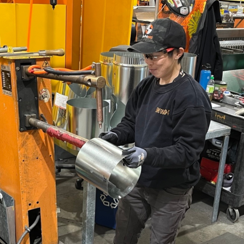 Image shows Rebecca Suen, sheet metal apprentice, working in a sheet metal fabrication shop.